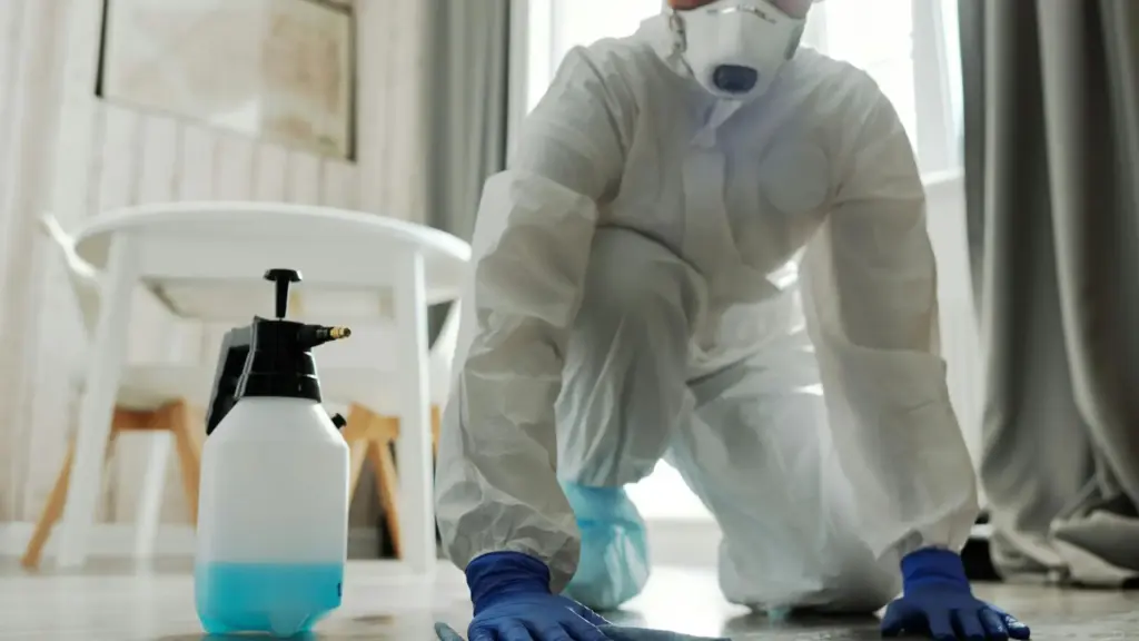 Water damage restoration technician in a hazmat suit and respirator cleaning a residential floor.